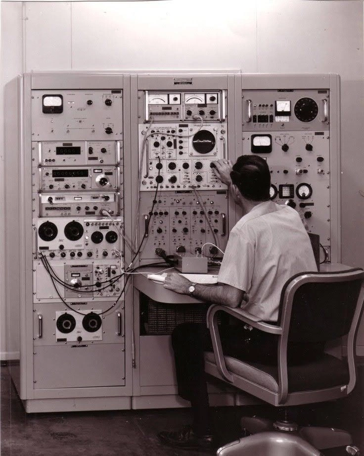 An operator seated at a bank of analogue instruments and controls.